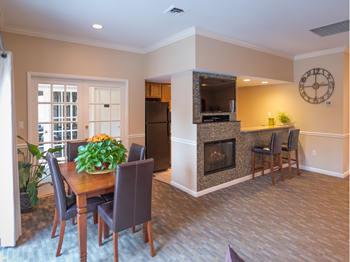 resident lounge at Versailles apartments in Towson, MD with table and chairs, wall mounted TV, fireplace and kitchen